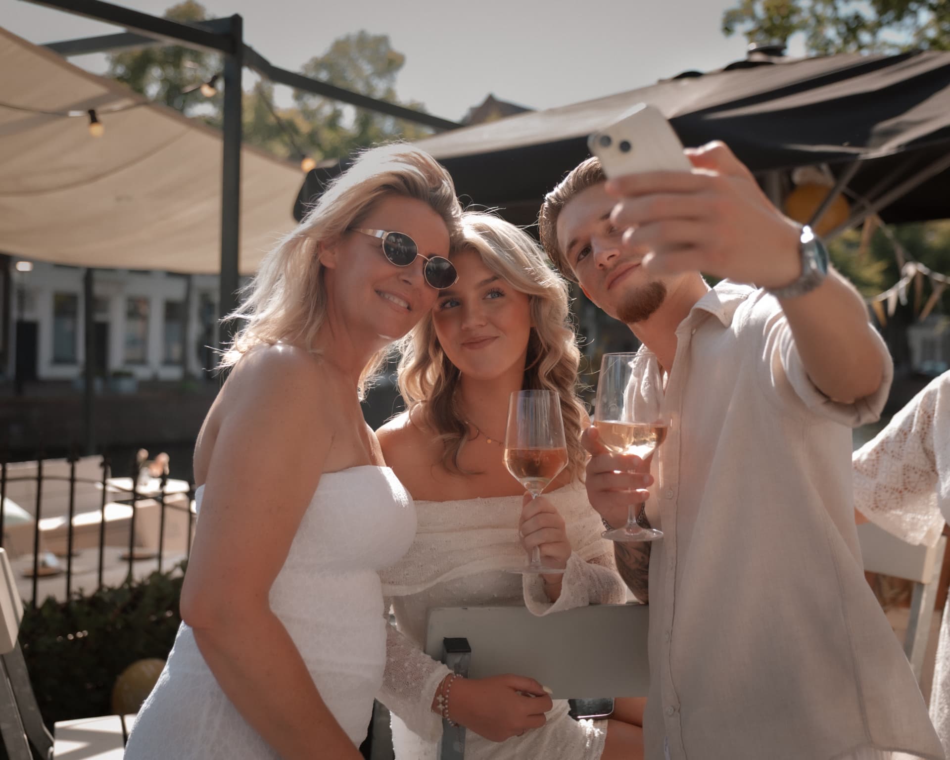 Drie mensen maken samen een selfie met een glas rosé op een zonnig terras.