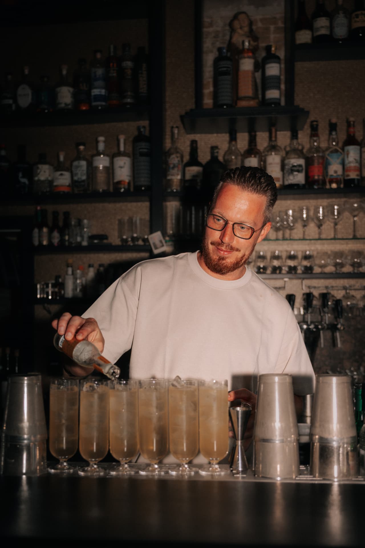 Een bartender schenkt champagne in een rij glazen achter een stijlvolle bar.